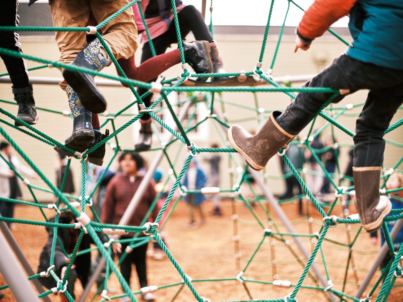 Children climbing an outdoor rope structure in rain boots